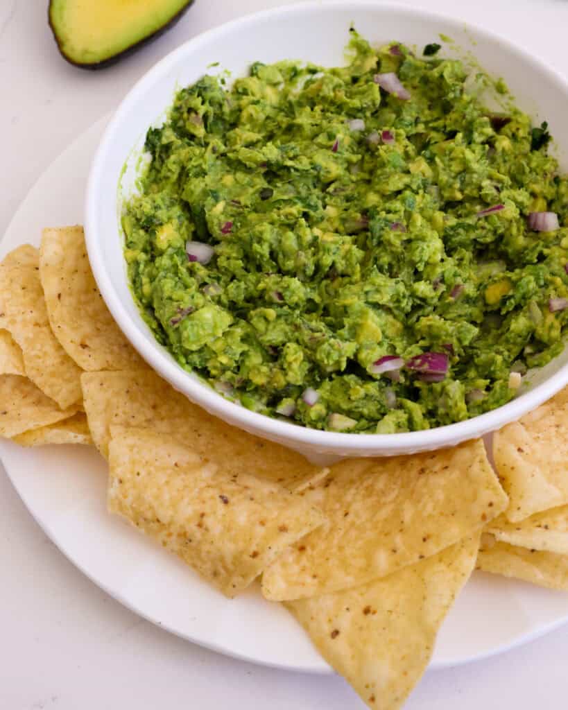 A bowl full of guacamole with tortilla chips on the side.