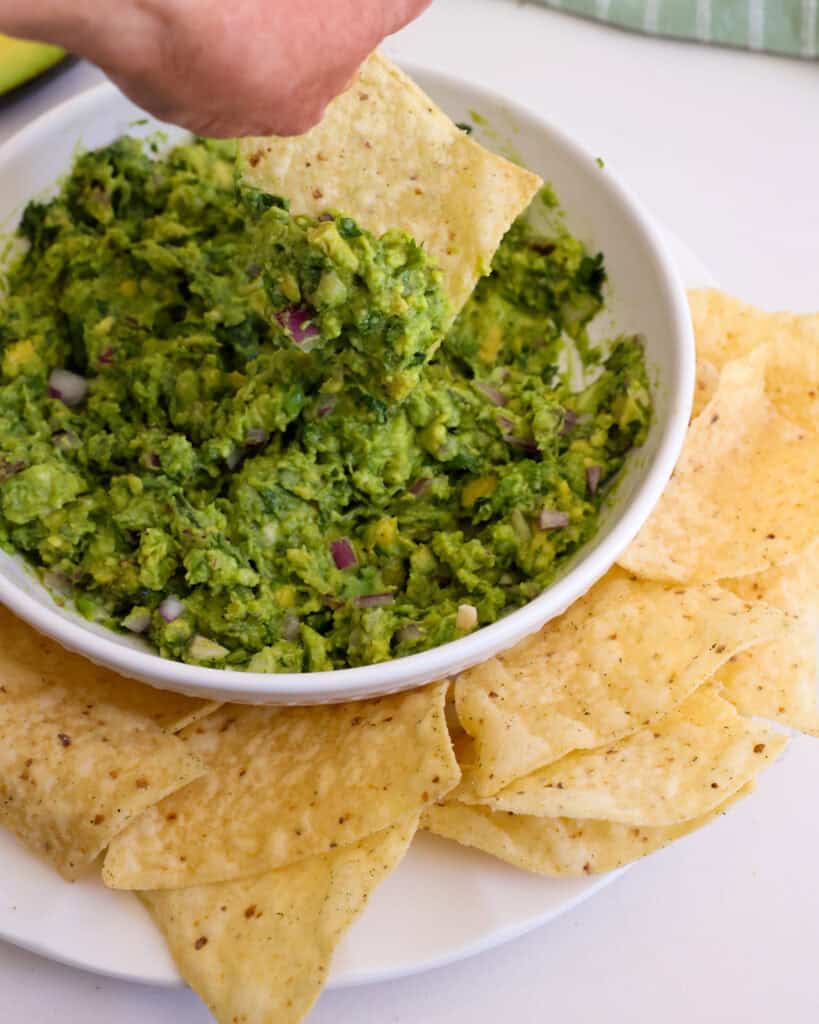 A bowl of guacamole with a tortilla chip dipped in it.
