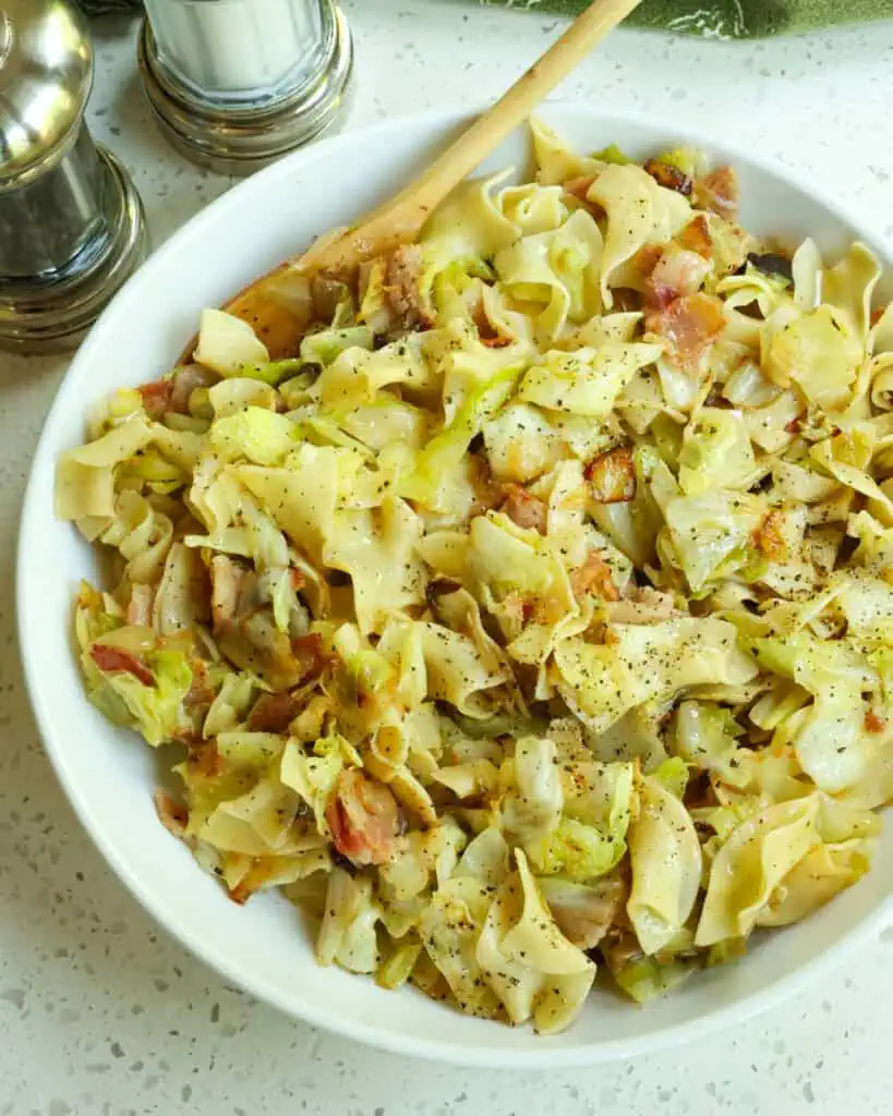A bowl full of haluski (cabbage and noodles) with a salt and pepper shaker in the background. 