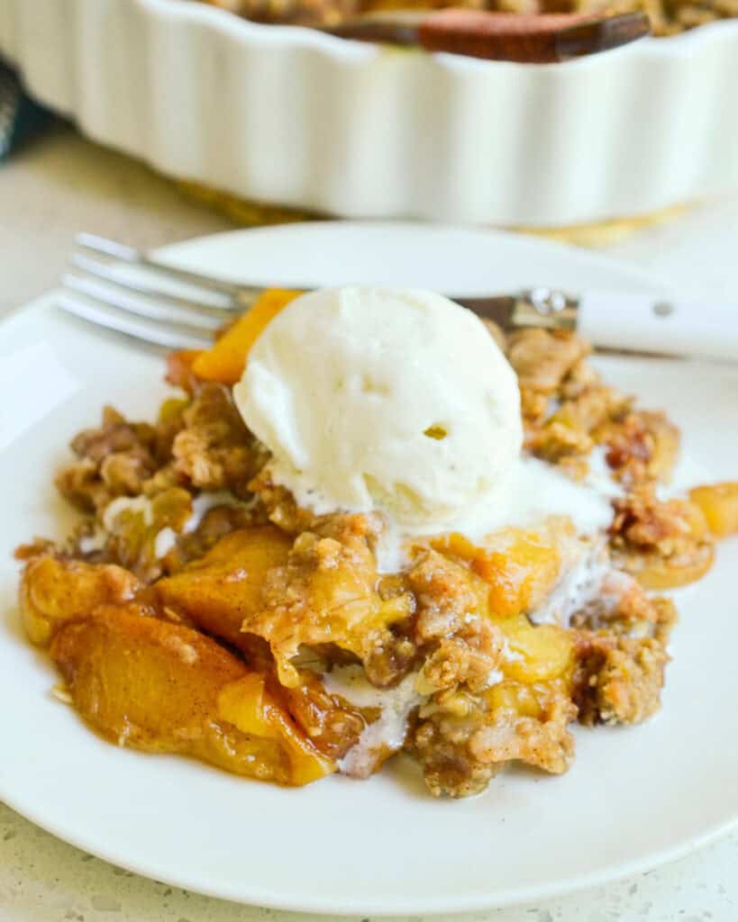 Peach crisp on a plate with juicy peaches soaked in a sweet cinnamon syrup and topped with a crispy crumble topping.