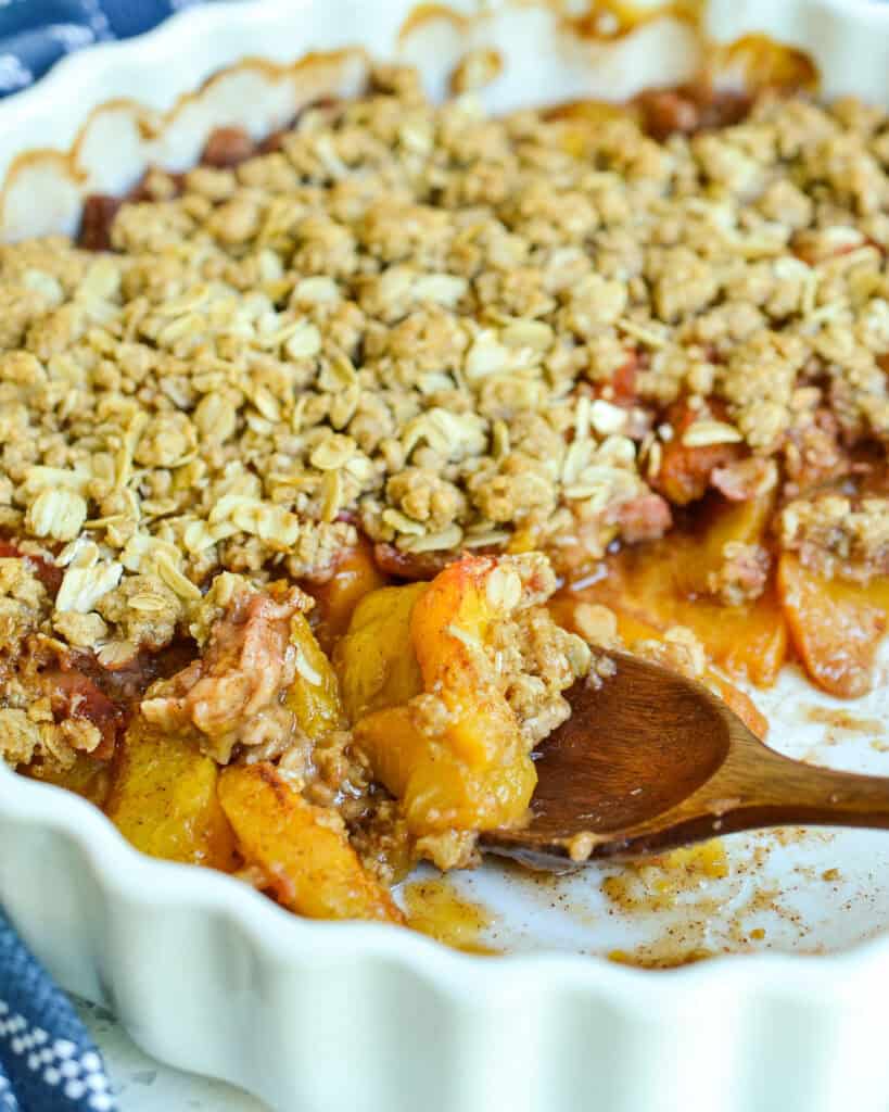 Close up view of peach crisp with some on a wooden spoon.