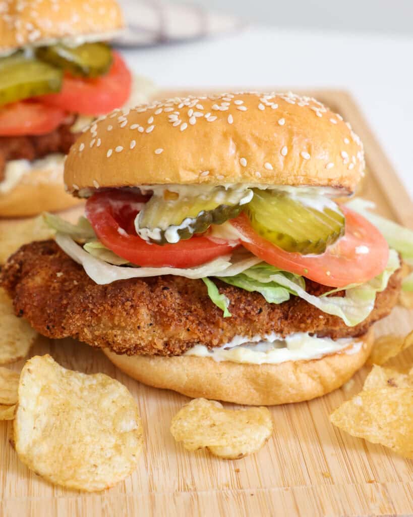Fried pork tenderloin sandwich on a bun with mayo, lettuce, tomato, and pickle. 