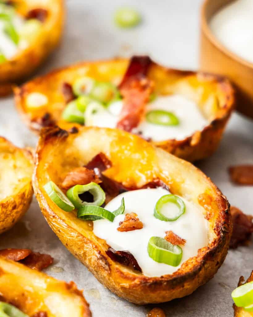 A close up view of two potato skins with cheese, bacon, sour cream, and green onions in them. 