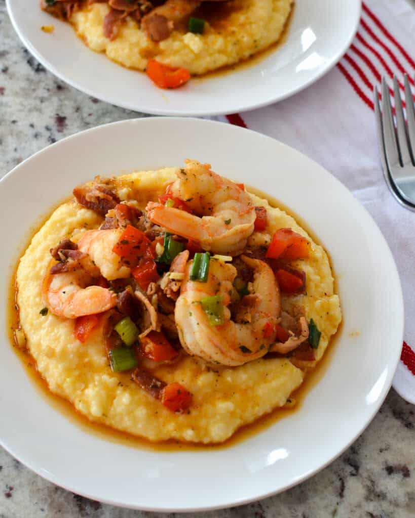 Shrimp and Grits Overhead view of shrimp and grits with bacon, bell peppers, and green onions on a white single serving plate.