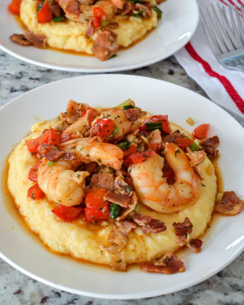 Shrimp and Grits Shrimp and grits on a single serving plate with two forks and a read and white towel in the background.