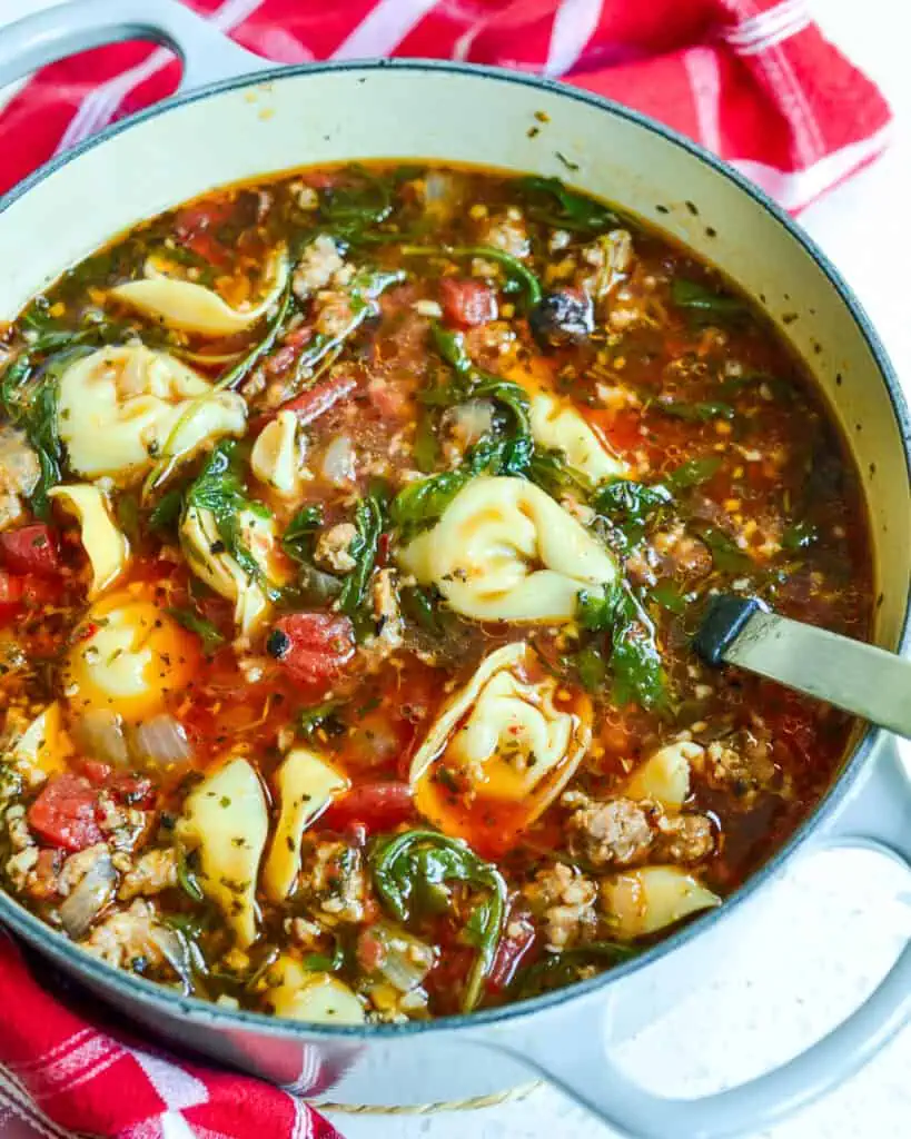 A large dutch oven full of cheese tortellini, sausage, and arugula soup with a soup ladle in it. 