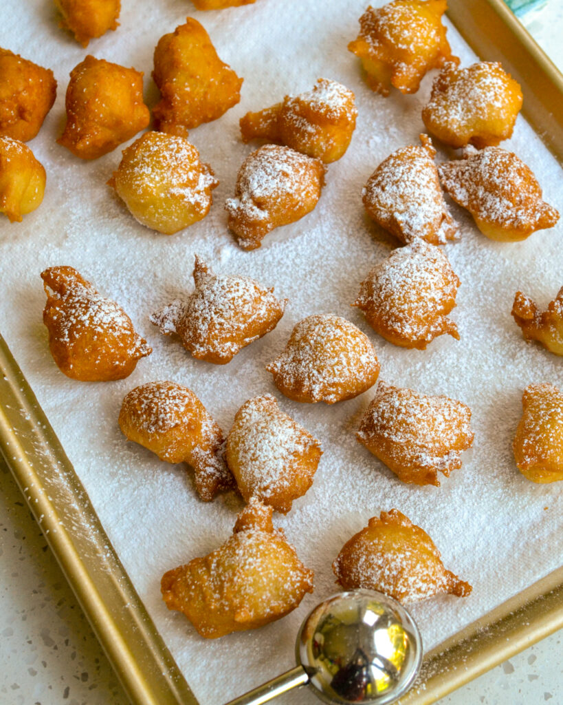 Zeppole on paper towels sprinkled with powdered sugar.