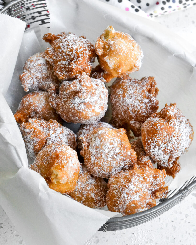 Fried zeppoles coated with powdered sugar in a wire basket lined with parchment paper.