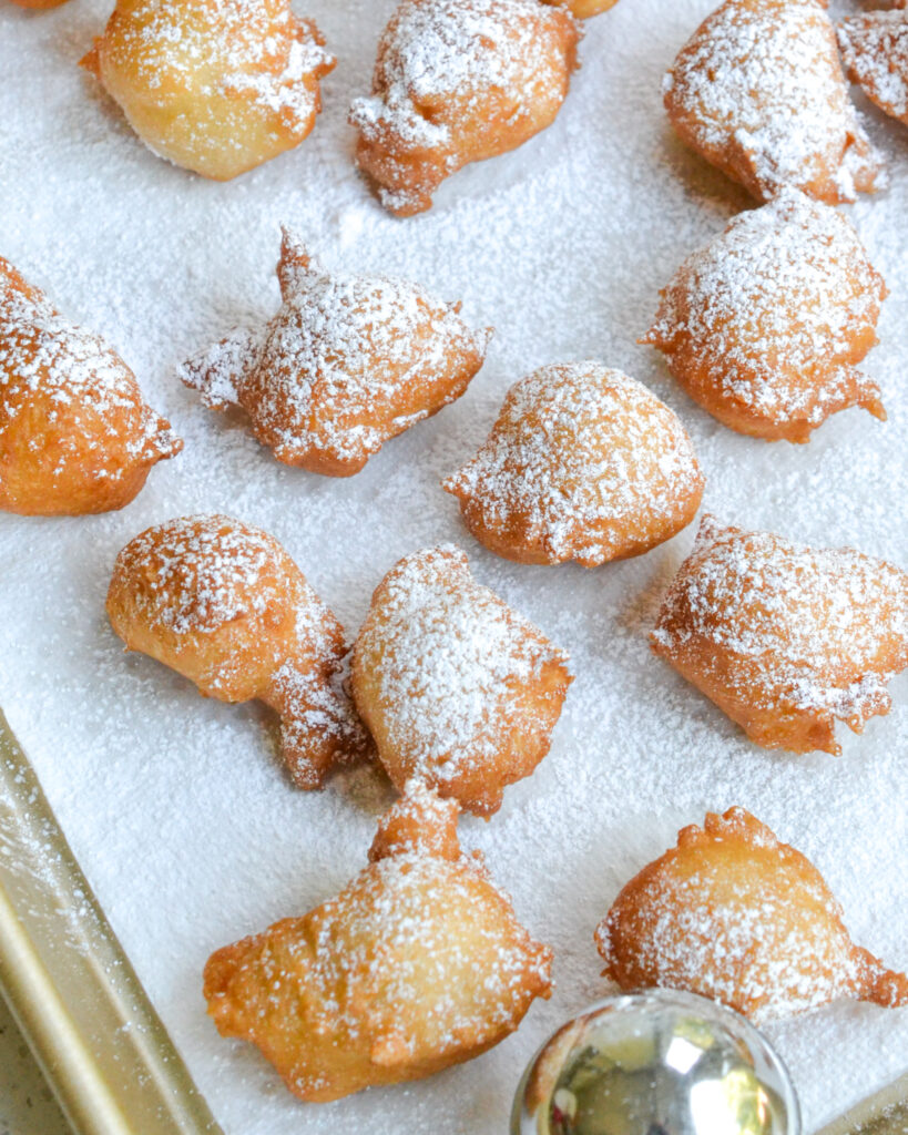 Fried zeppoles sprinkled wiht powdered sugar on a paper towel lined baking sheet.
