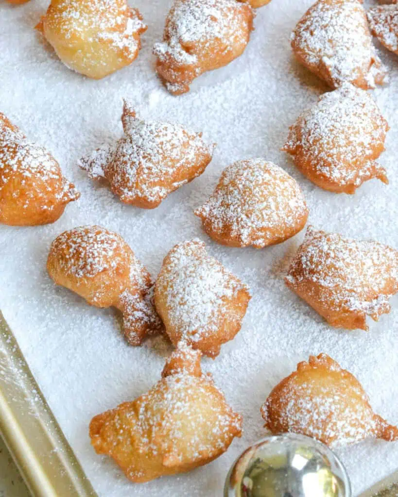 Fried zeppoles sprinkled wiht powdered sugar on a paper towel lined baking sheet. 