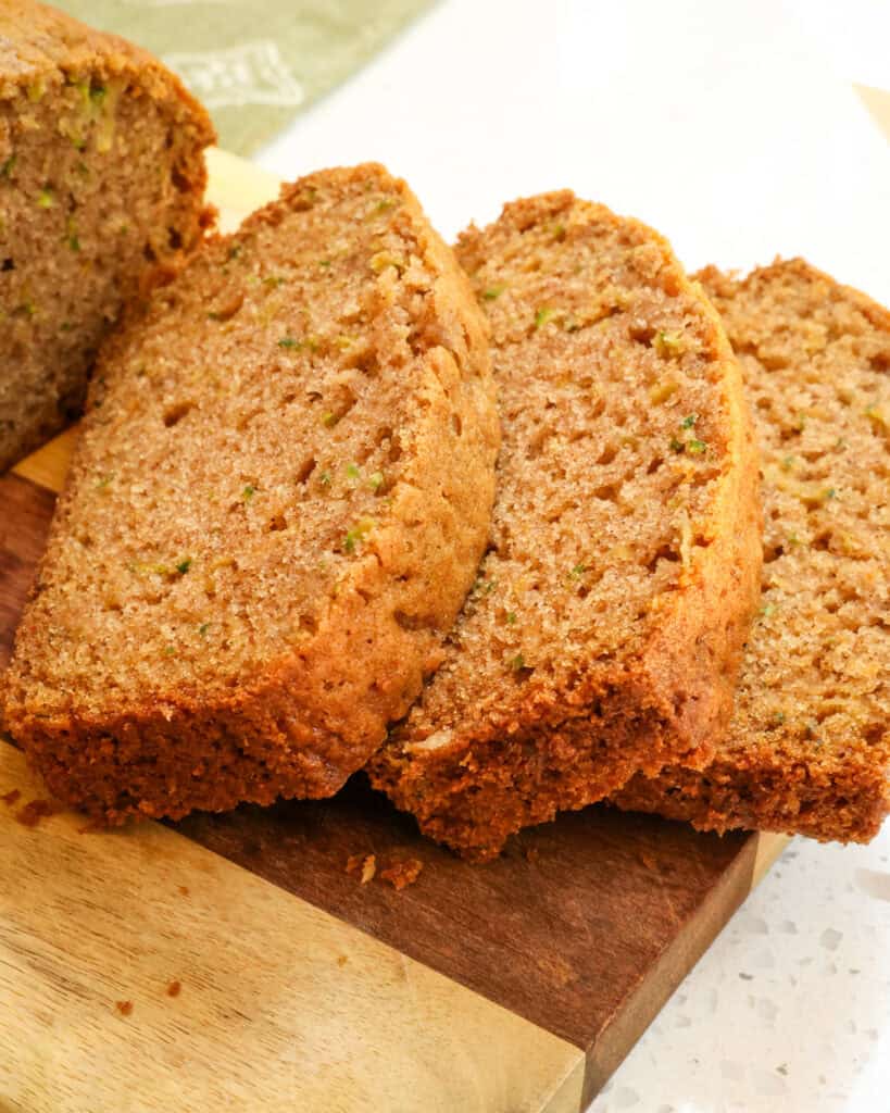 Three slices of zucchini bread on a wood cutting boards.