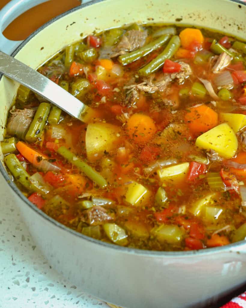 A Dutch oven full of beef vegetable soup with a large ladle in it.