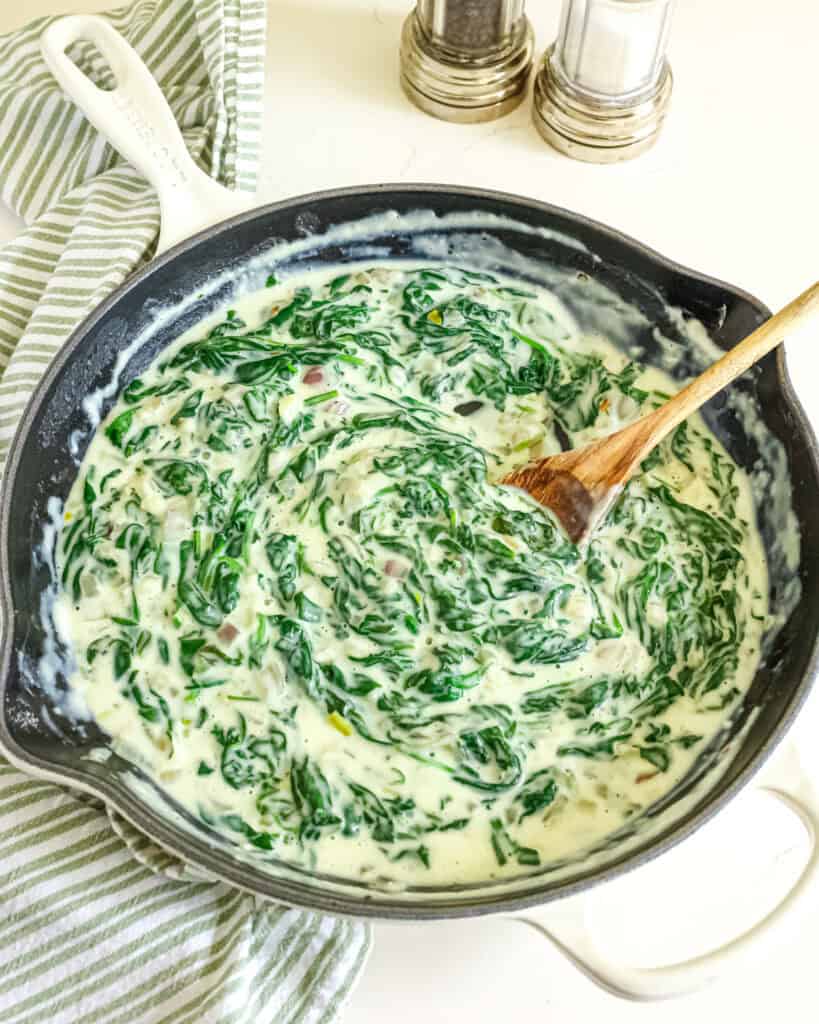 Creamed spinach in a skillet with salt and pepper shakers in the background.