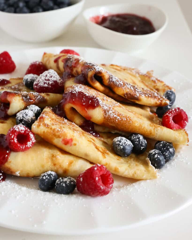 Layered crepes on a plate with raspberry jam and powdered sugar. 