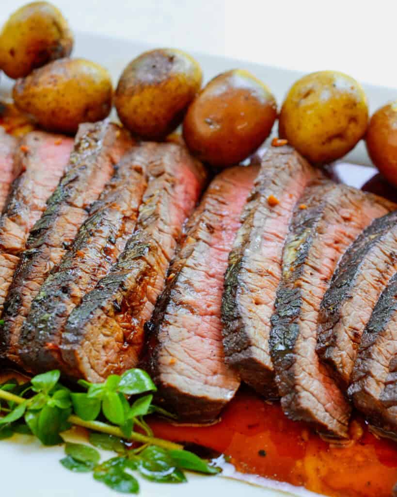Sliced london broil steak on a plate with baby Yukon gold potatoes.