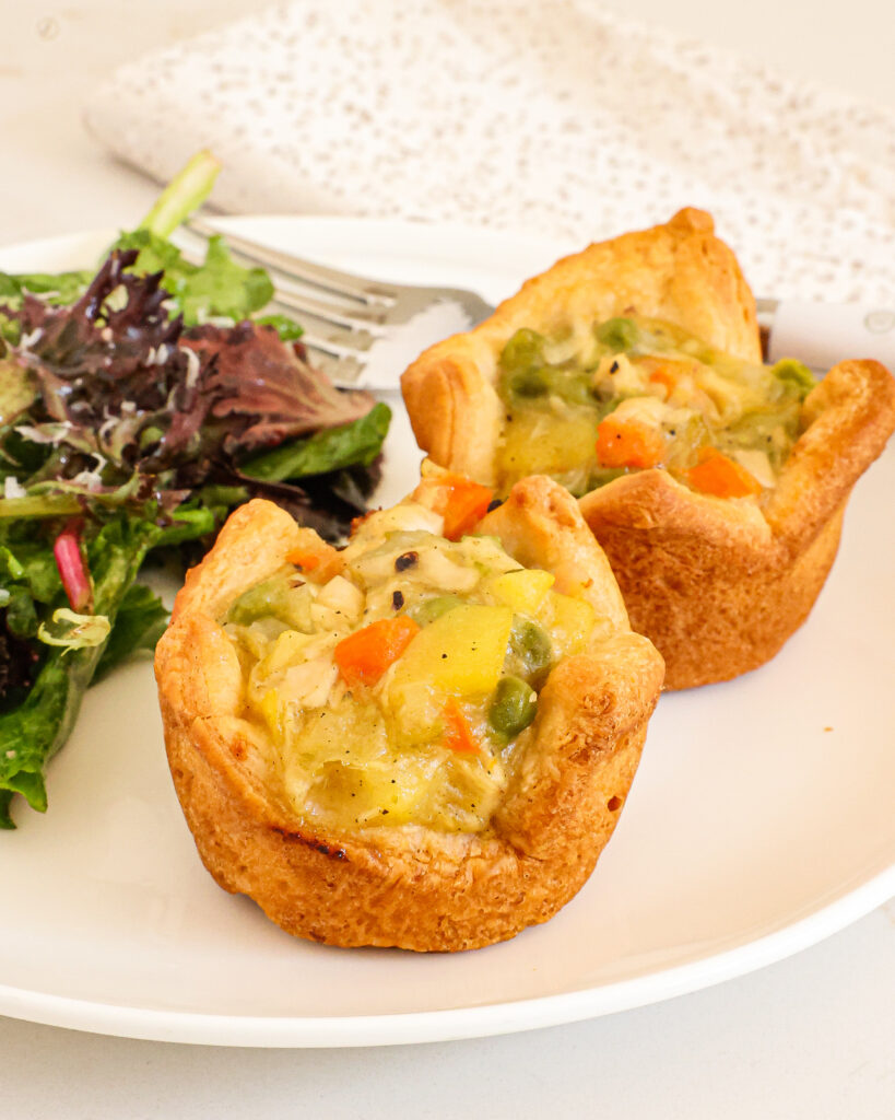 Two mini chicken pots pies on a plate with mixed spring greens.