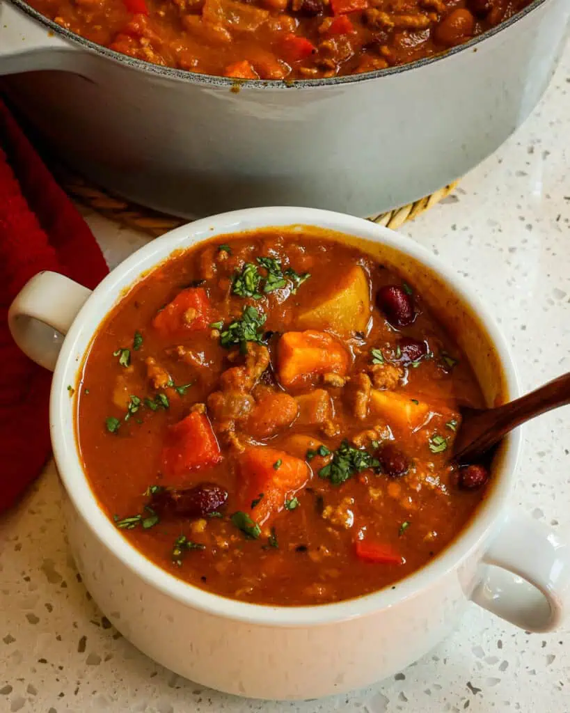 A bowl full of pumpkin chili in front of a Dutch oven full of pumpkin chili. 
