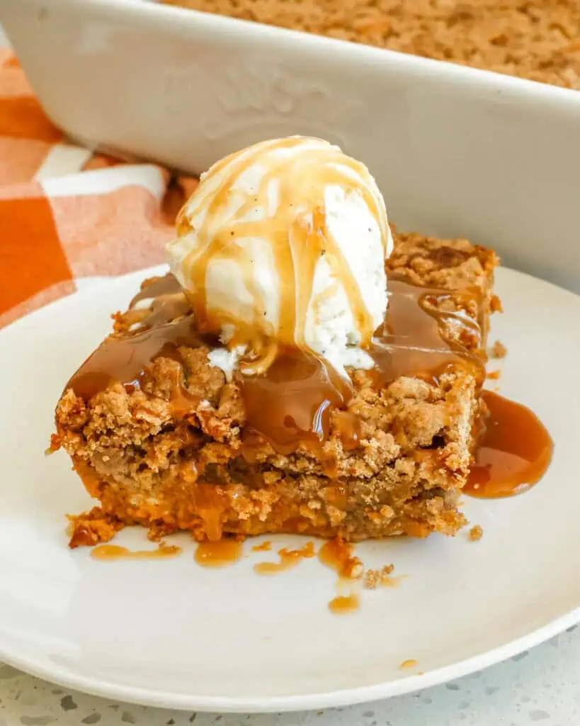 A pumpkin of pumpkin dump cake with a scoop of vanilla ice cream and caramel sauce on top.