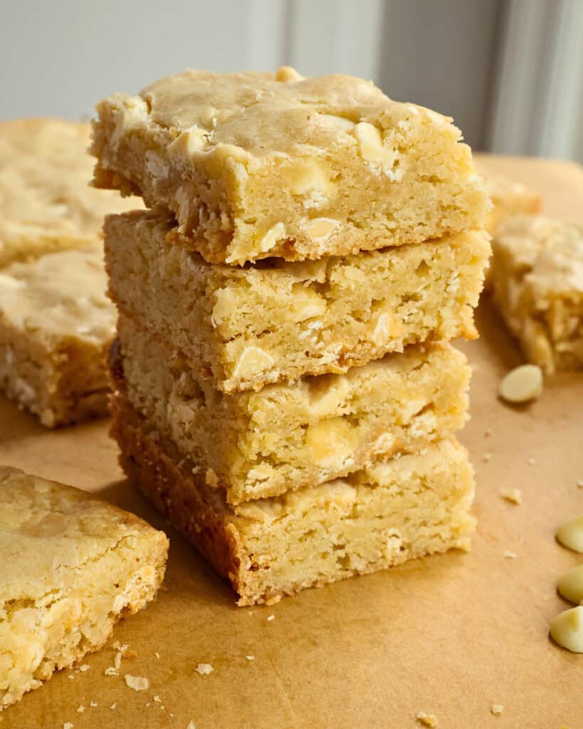 A close up view of stacked Blondies with white chocolate chips scattered.