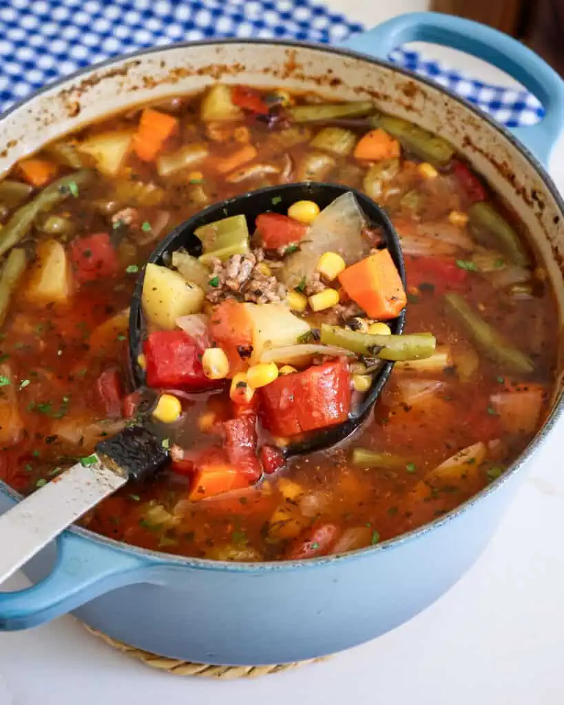 A Dutcch oven and a ladle full of hamburger soup. 