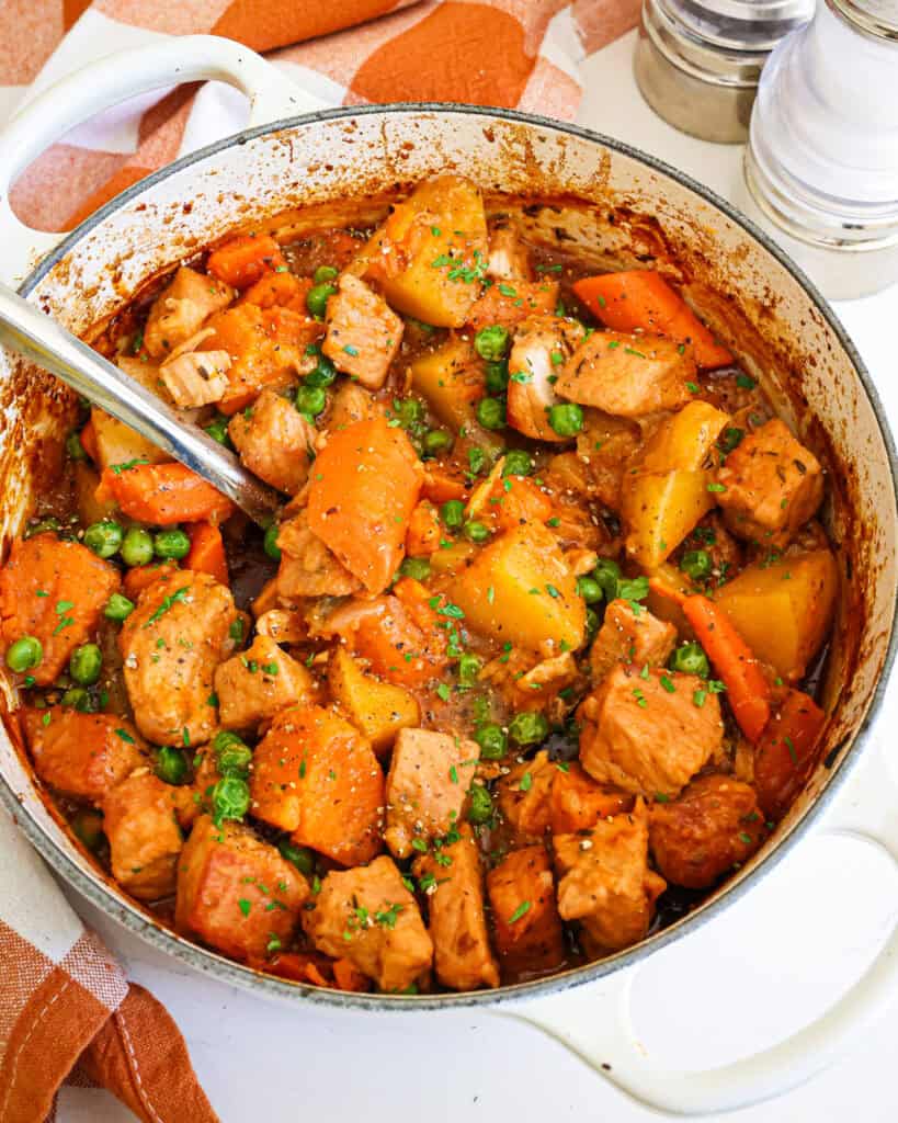 An overhead view of pork stew in a large Dutch oven with a salt and pepper shaker in the background.