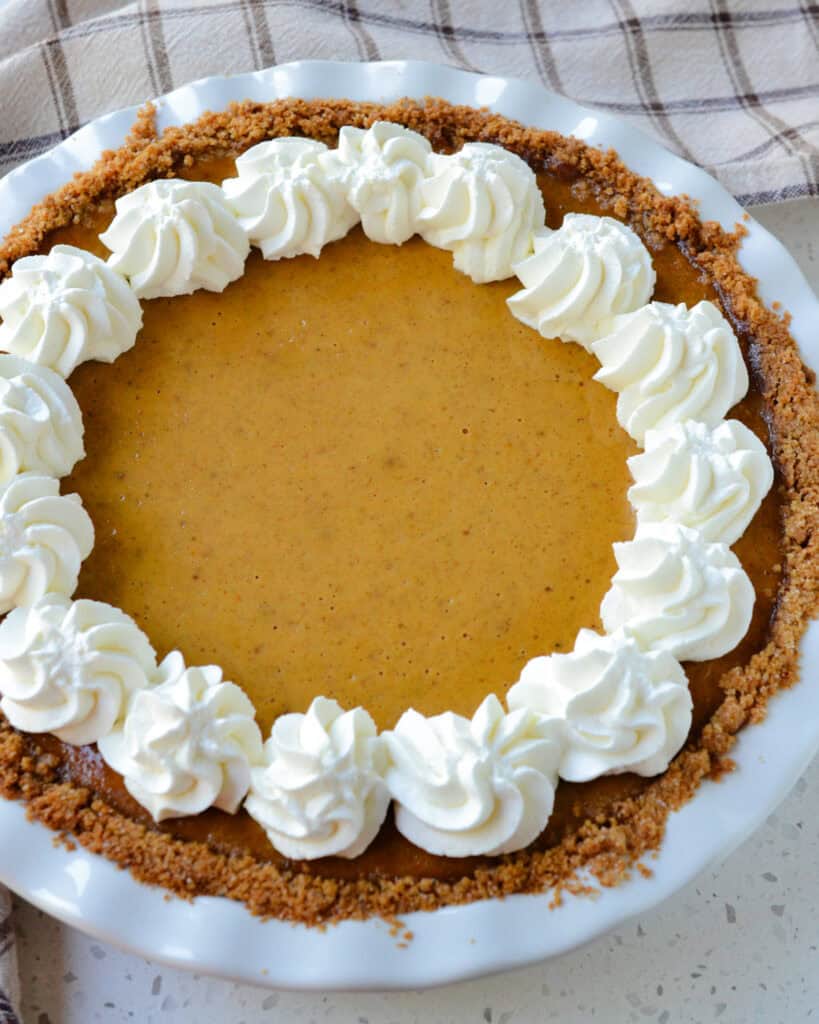 An overview of homemade pumpkin pie with graham cracker crust and whipped cream. 