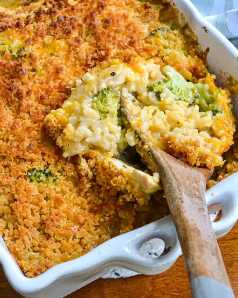 A large casserole dish full of chicken broccoli rice casserole. with a wooden spoon in the casserole. 