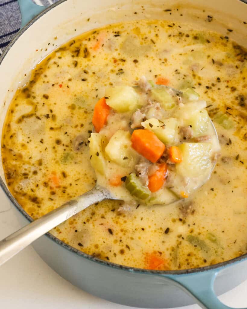 Sausage and potato soup in a Dutch oven with a ladle in it.