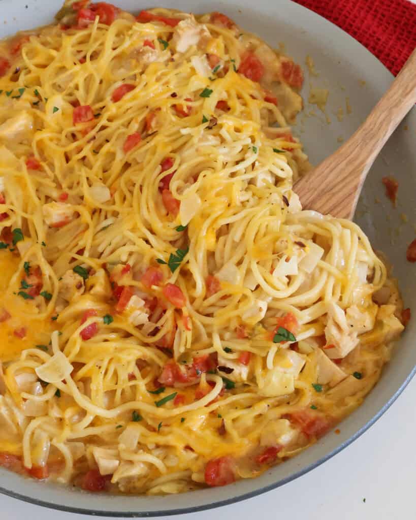 Chicken spaghett in a large skillet with a wooden spatula.