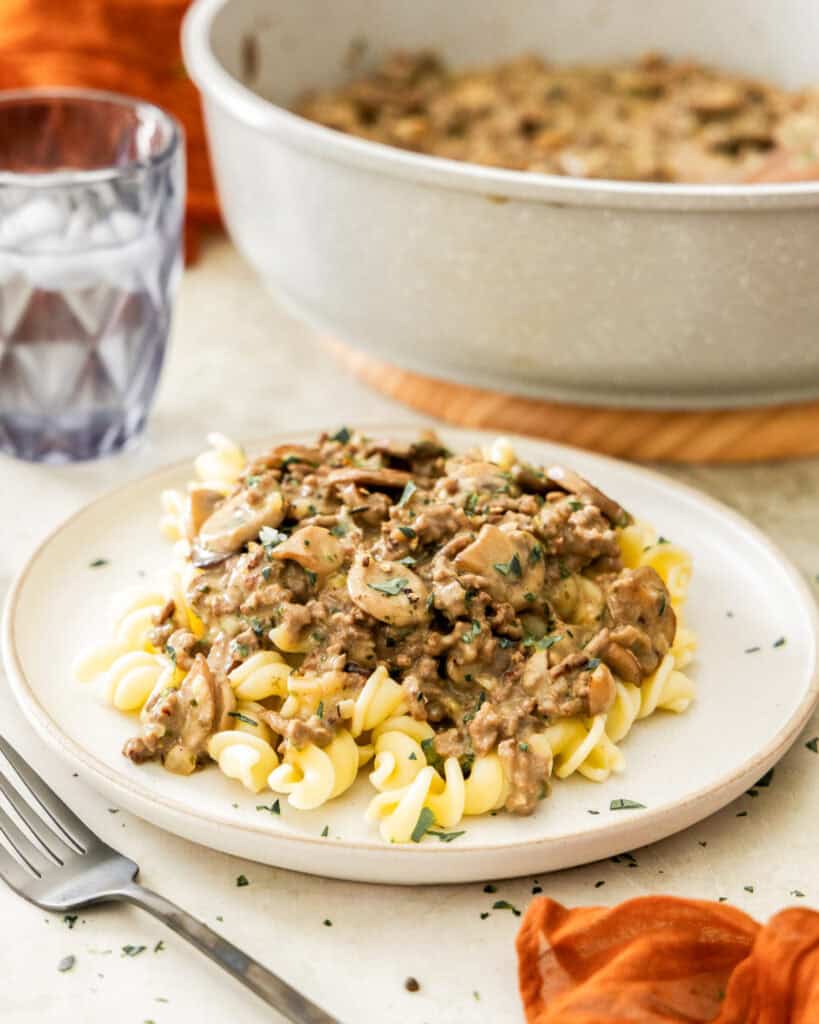 A plate full of ground beef stroganoff with a skillet full of it in the background.