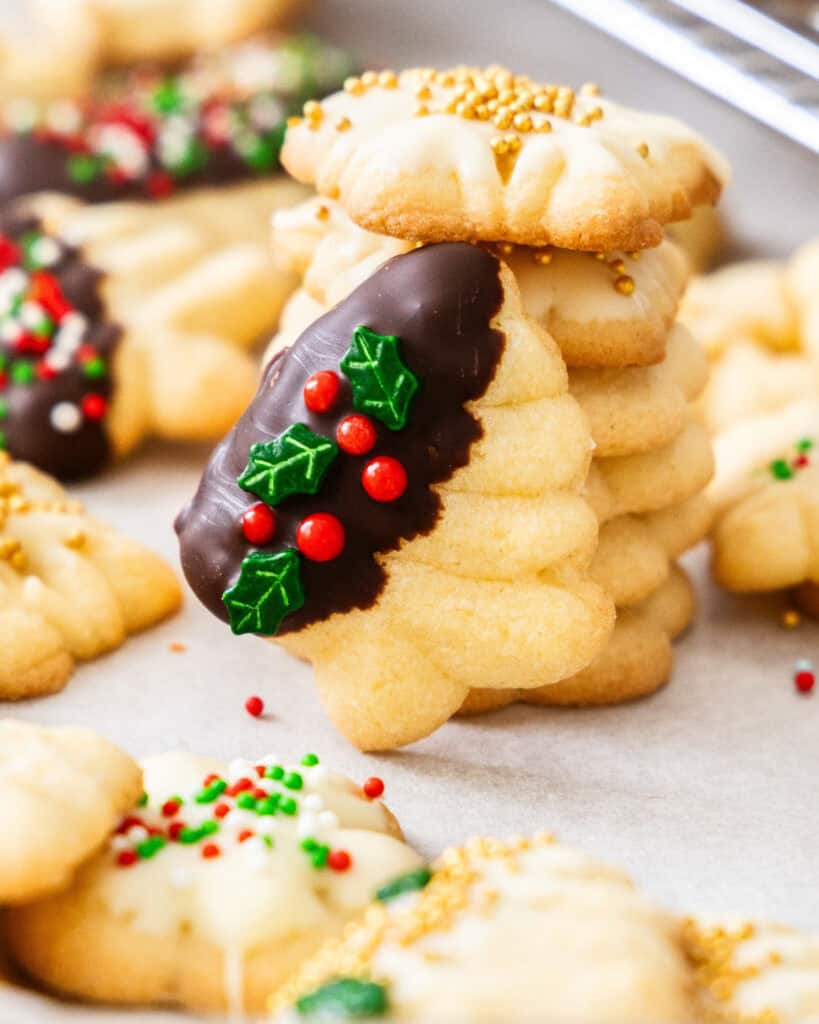 A spritz Christmas tree cookie leaning against a stack of spritz star cookies with gold pearls. 