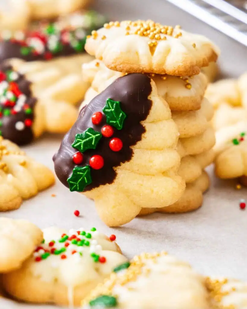 A spritz Christmas tree cookie leaning against a stack of spritz star cookies with gold pearls.