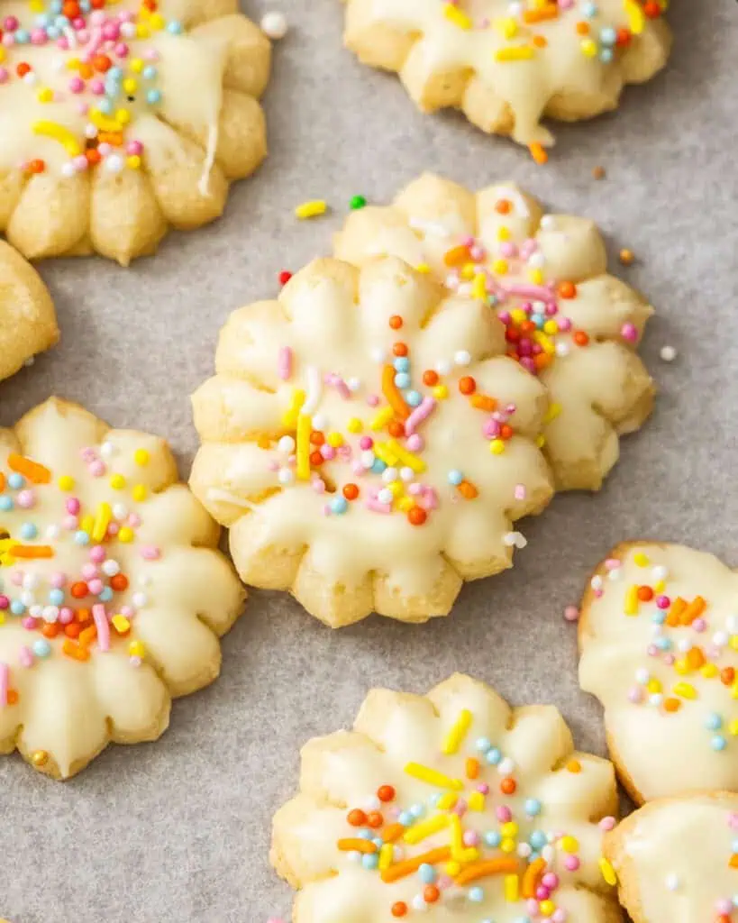 A close up view of sunflower spritz cookies dipped in white chocolate with rainbow sprinkles.