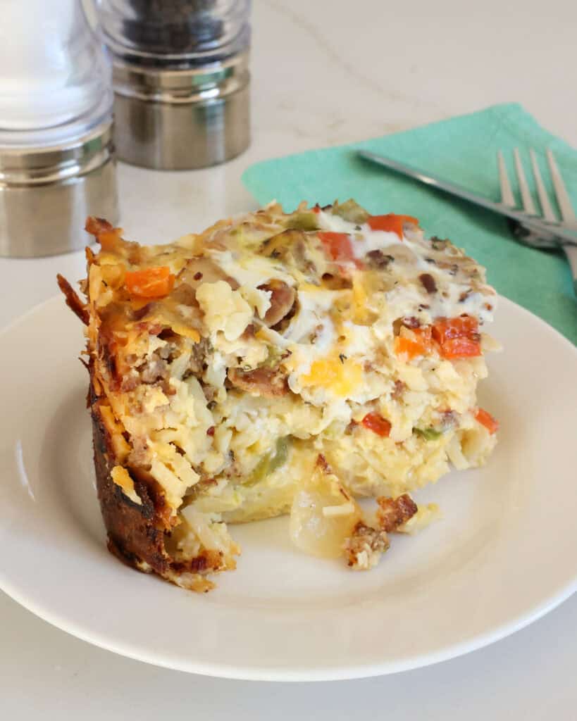 A piece of crock pot breakfast casserole on a plate a napkin and silverware in the background. 