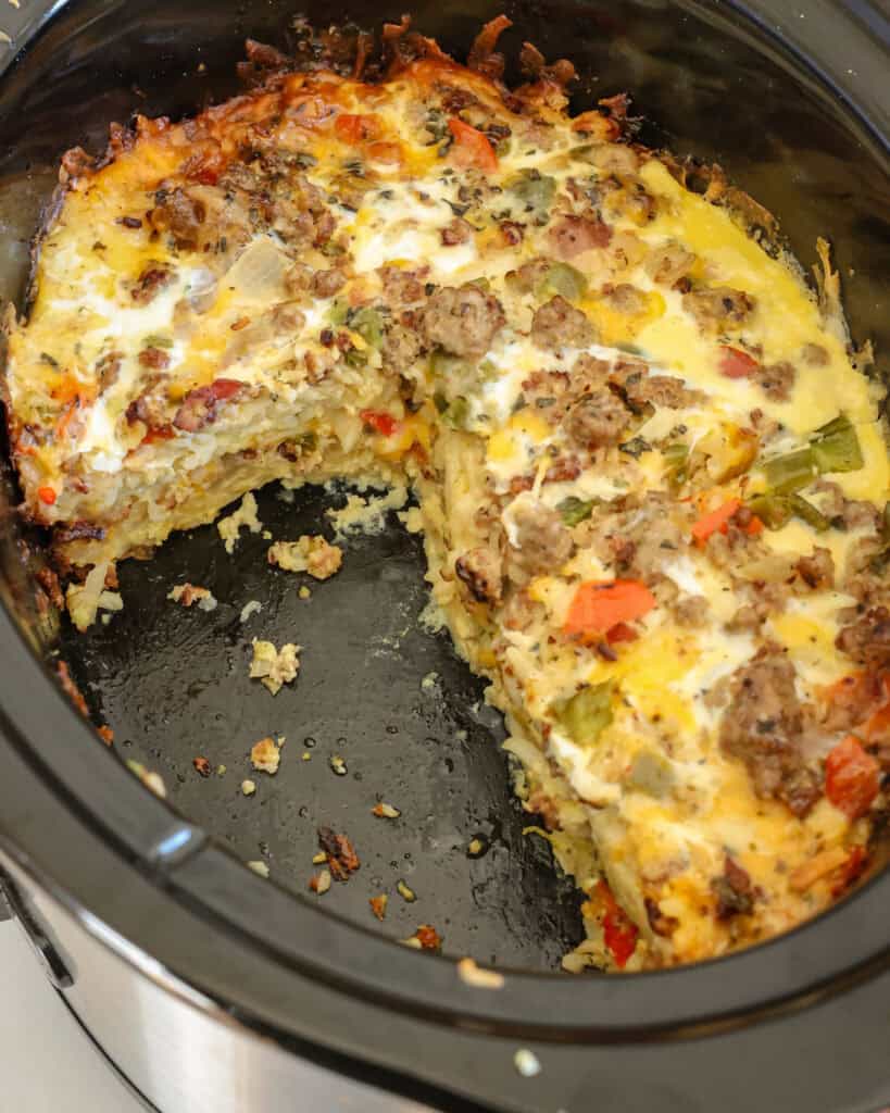 An overhead view of breakfast casserole with sausage, bacon and bell peppers in a crock pot. 