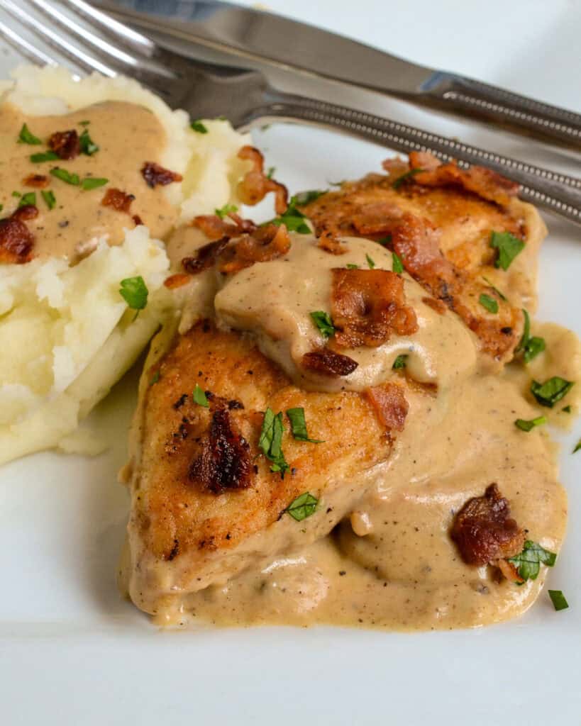 Smothered Chicken on a white plate and mashed potatoes behind.