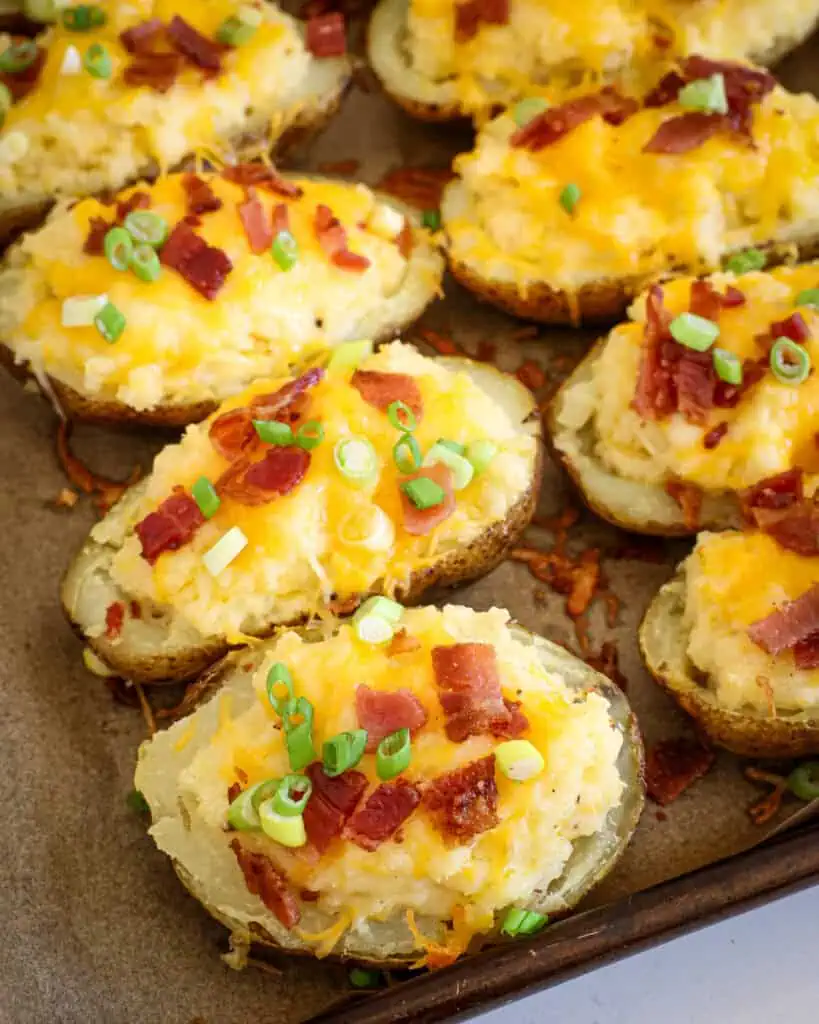 A close up view of twice-baked potatoes on a parchment paper covered baking sheet. 