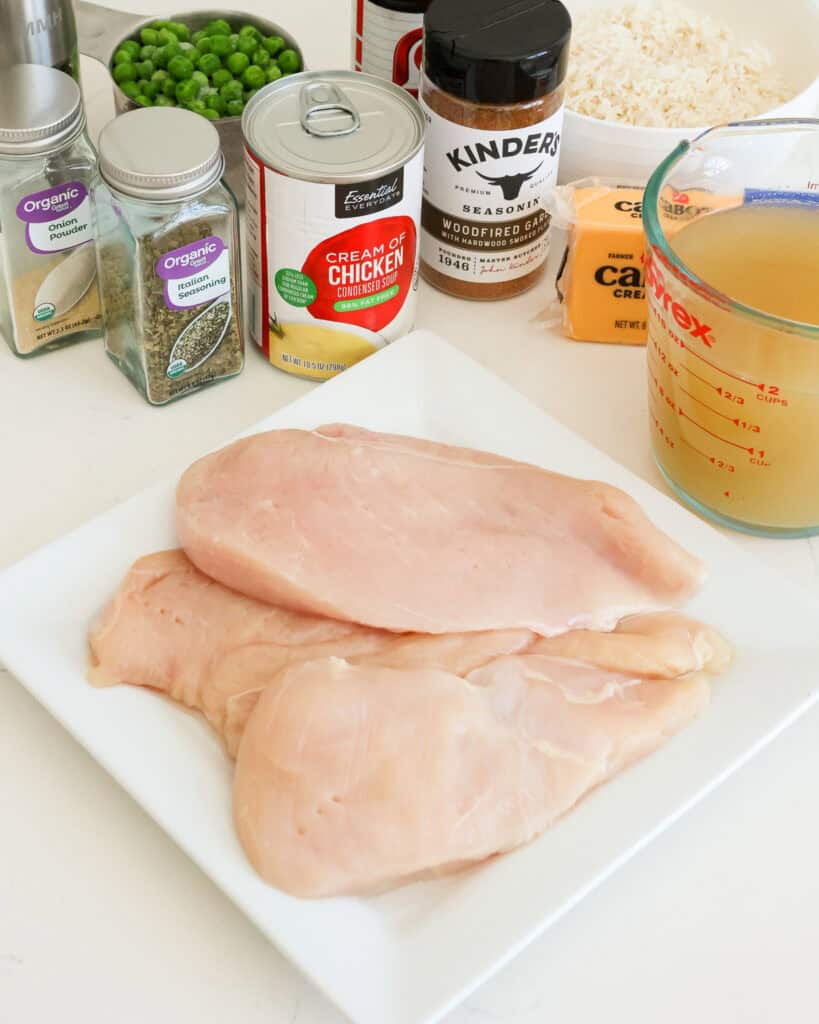 Al the ingredients for cheesy chicken and rice casserole, chicken broth, cream of chicken soup, Italian seasoning, seasoned salt, garlic powder, onion powder, black pepper, long grain white rice, frozen peas, chicken breasts, and cheddar cheese. 