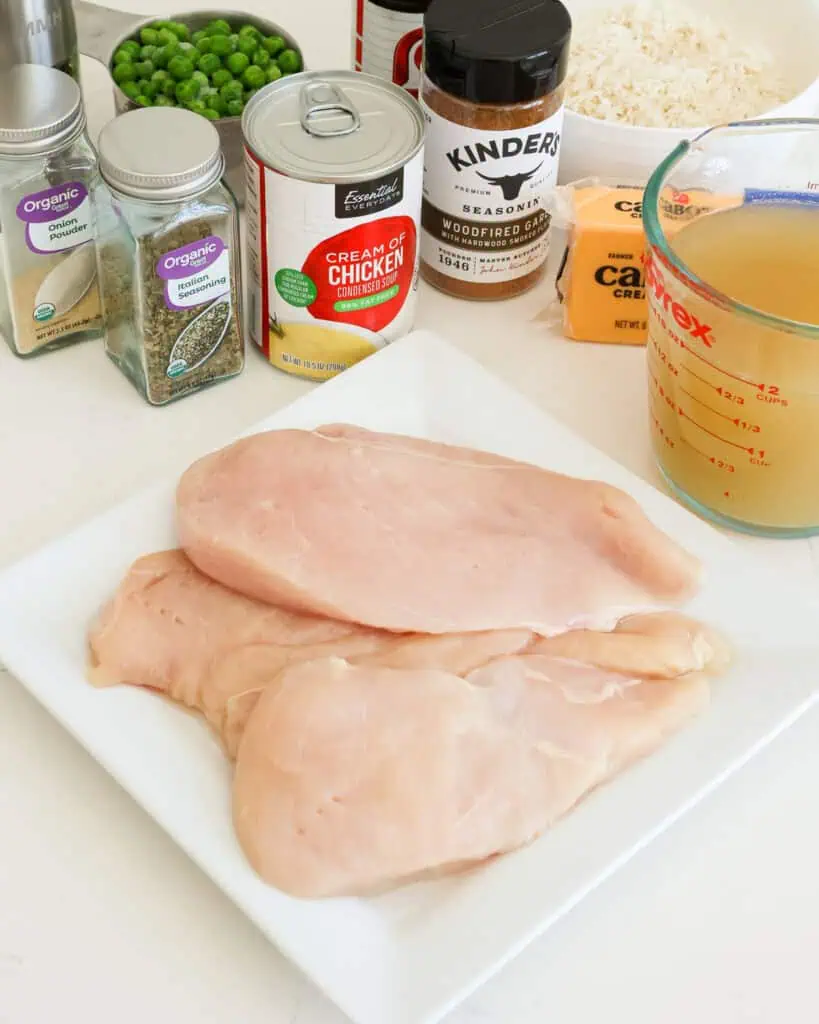 Al the ingredients for cheesy chicken and rice casserole, chicken broth, cream of chicken soup, Italian seasoning, seasoned salt, garlic powder, onion powder, black pepper, long grain white rice, frozen peas, chicken breasts, and cheddar cheese. 