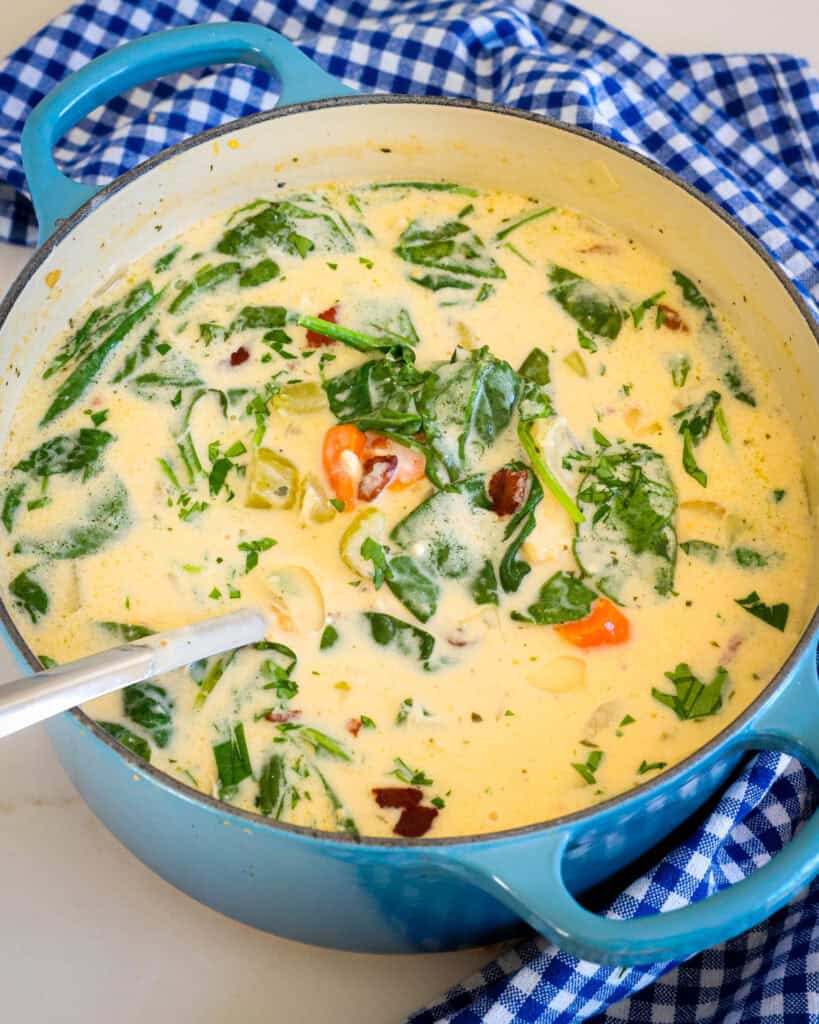 A Dutch oven full of crack chicken soup with bacon, onions, carrots, tender chicken, and ranch seasoning in a super creamy cheesy broth with spinach and sour cream. 