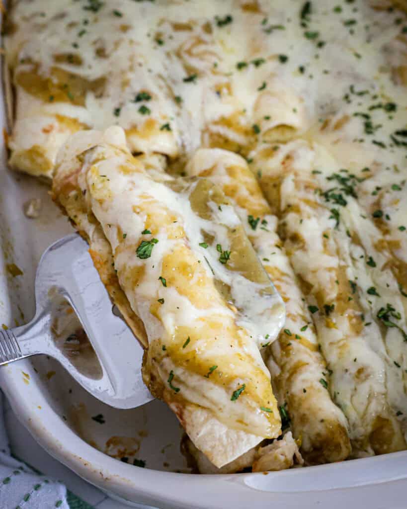 A spatula with one green chile chicken endchila over a dish full of them.