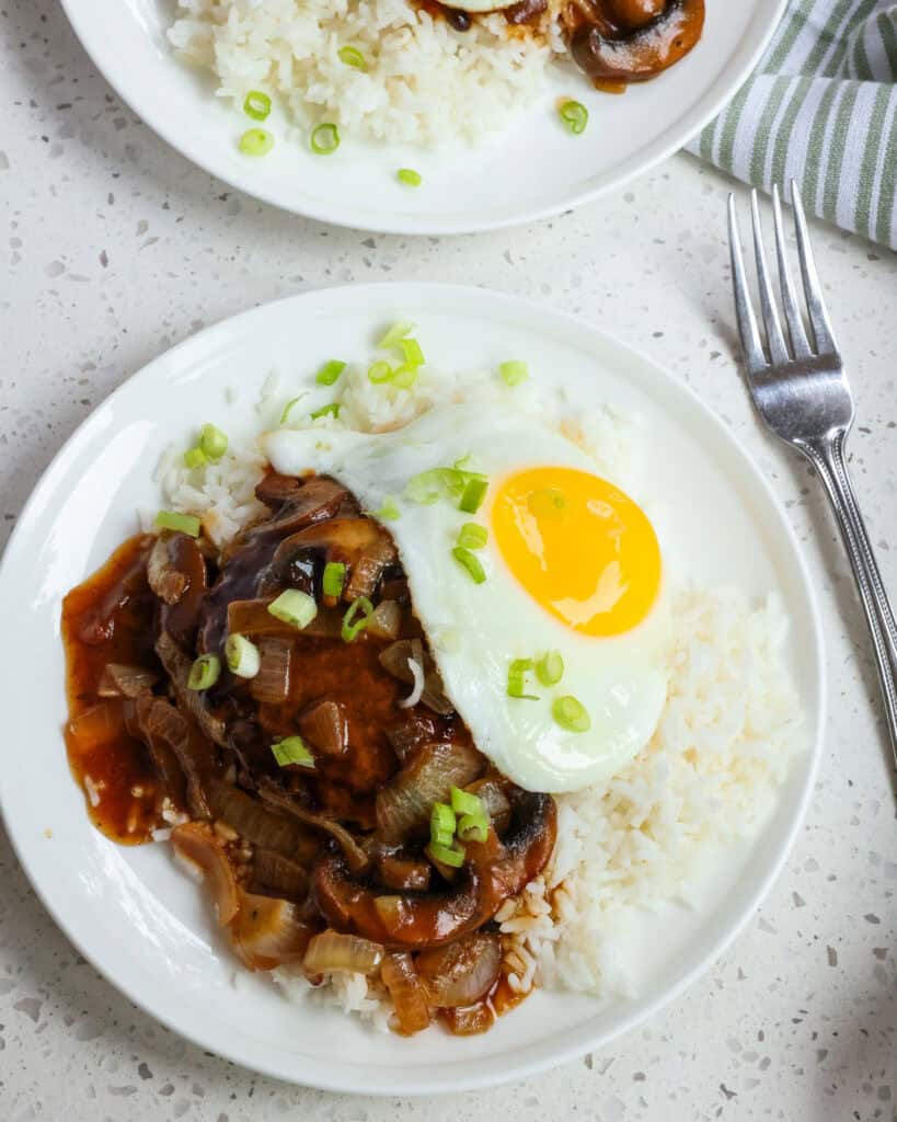 An overhead view of loco moco on a single serving plate with white rice and thin slices of green onion.