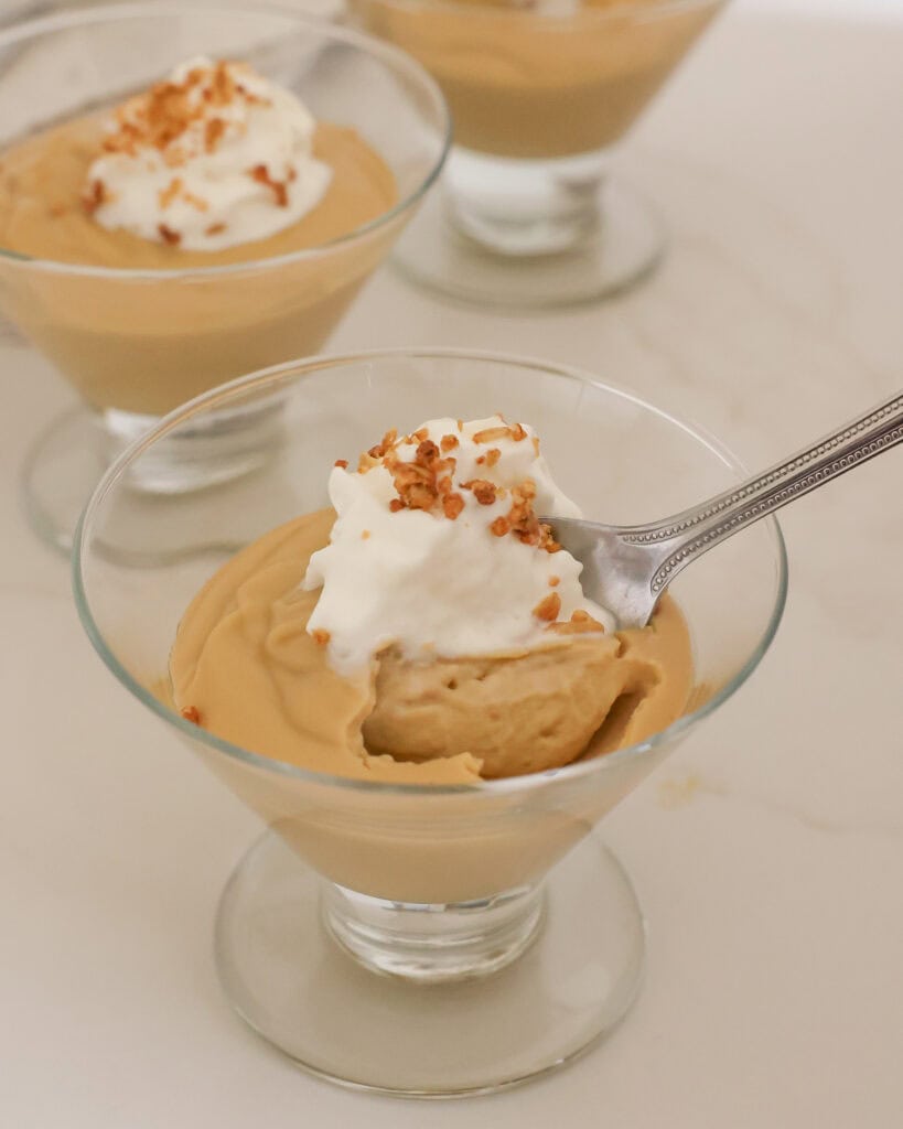 A sundae dish full of butterscotch pudding topping with whipped cream and a sprinkle of granola. 