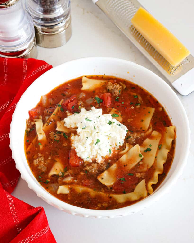 A serving bowl full of crock pot lasagna soup with salt and pepper shaker in the the back ground.