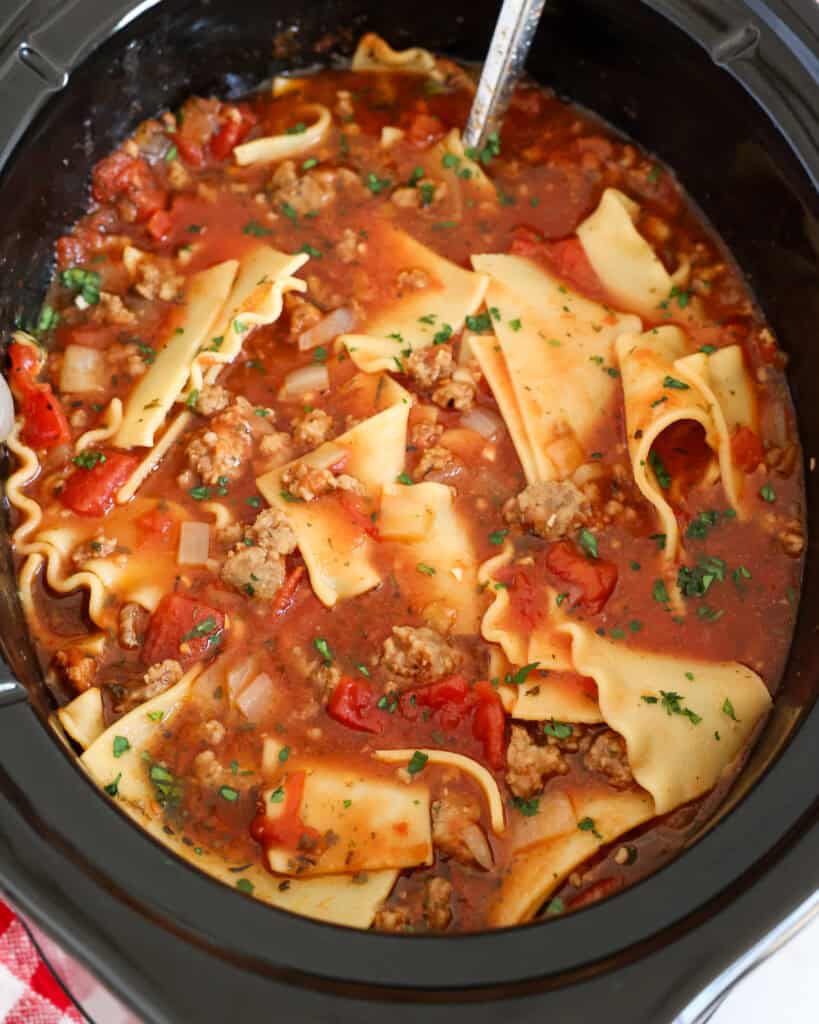 An overhead view of a crock pot full of lasagna soup with Italian sausage and tomatoes.