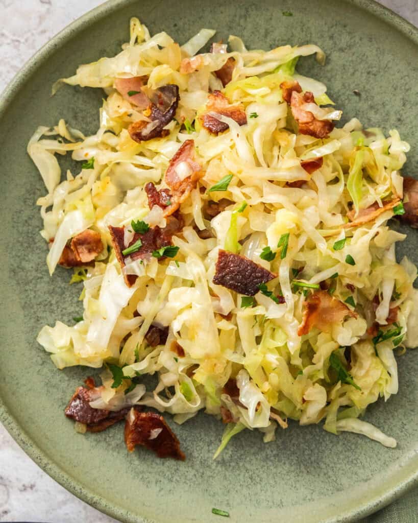 A close up view of fried cabbage with bacon on a plate.