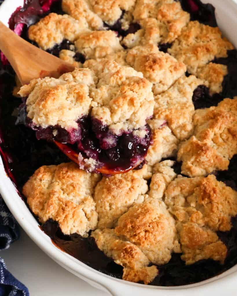 A baking and a spoon full of homemade blueberry cobbler.