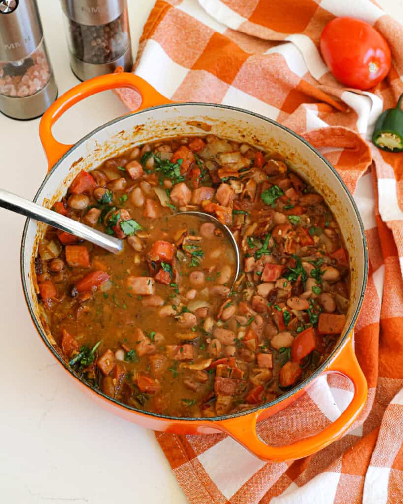A Dutch oven full of charro beans with ham, bacon, onions, jalapeno peppers, tomatoes, and spices.