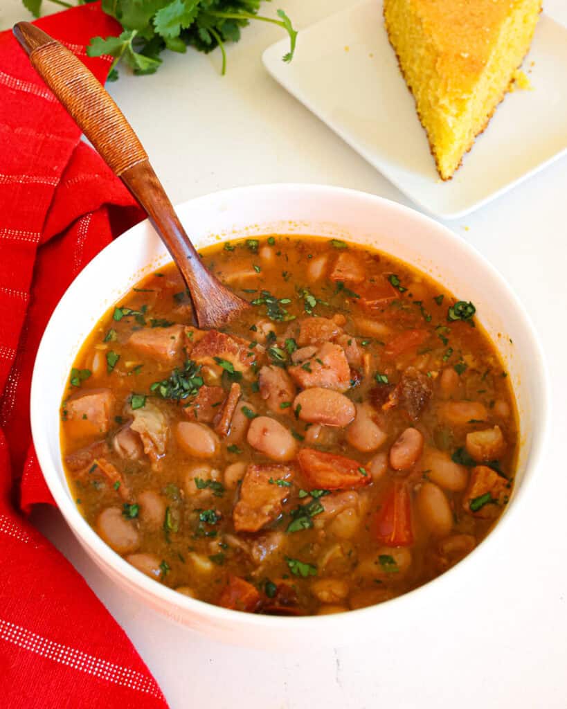 A single serving bowl full of charro beans with cornbread in the background.