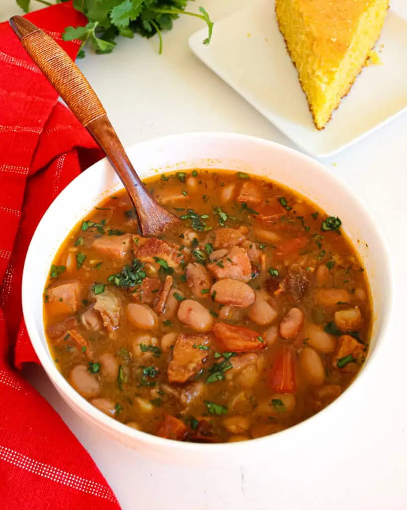 A single serving bowl full of charro beans with cornbread in the background. 